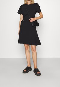 Czarna sukienka z krótkim rękawem, z rozkloszowanym dołem i akcentem w talii. Połączona z czarnymi butami wsuwanymi o teksturowanej podeszwie oraz małą torebką na ramię.