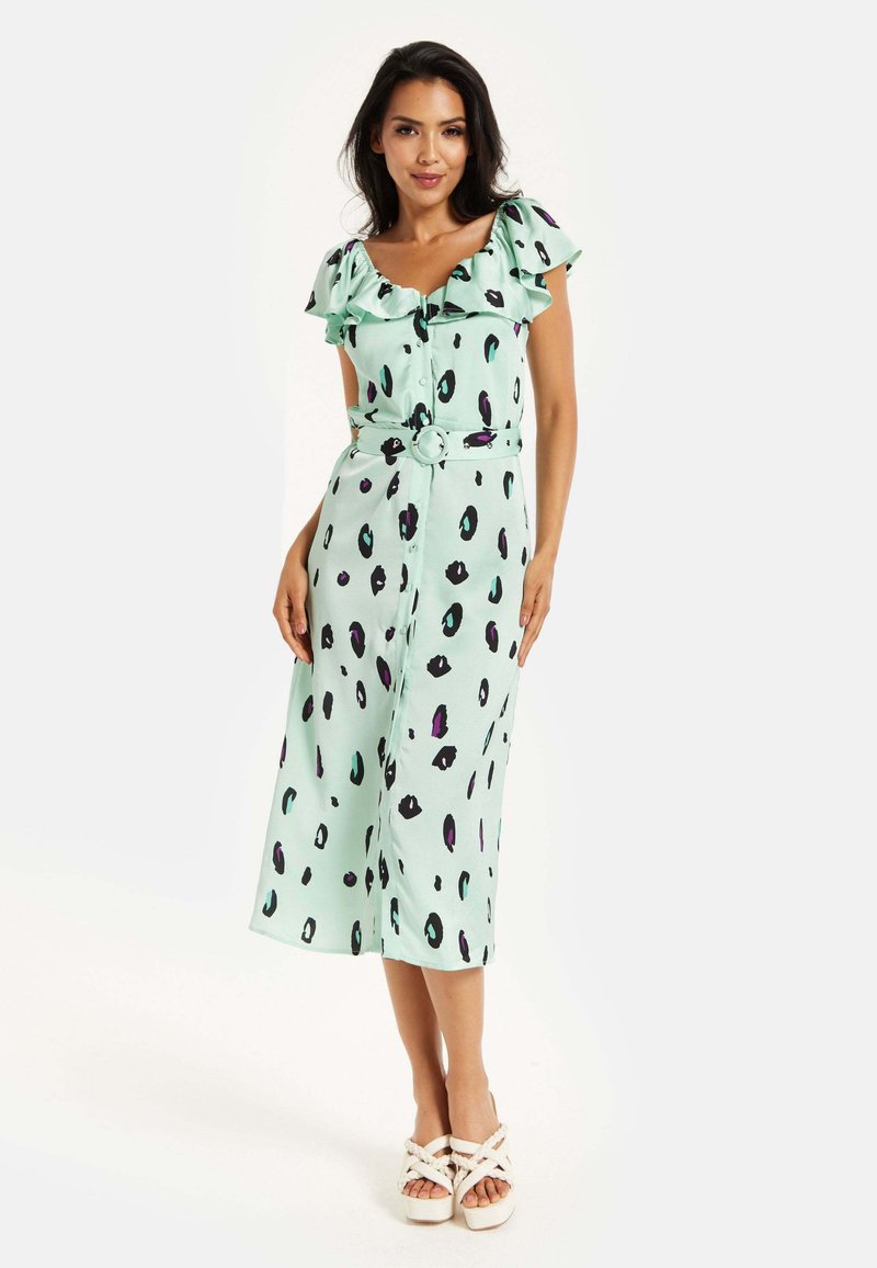 Mint green midi dress with ruffled cap sleeves, button front, belted waist, and black and purple abstract spots. Worn with white strappy sandals.