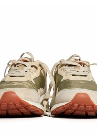 Zapatillas con parte superior en beige y oliva, materiales texturizados, cordones crema y suela de goma con acentos en naranja. Presenta un diseño de punta redondeada.