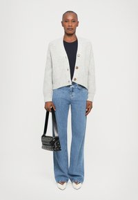 Cardigan grigio a maglia con tre bottoni, top blu navy, jeans a gamba larga azzurri e una borsa nera con borchie argentate. Scarpe bianche con punta.