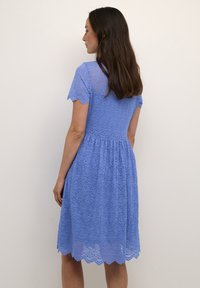 Lacekjole i lyseblå med korte ærmer, scallopkant og blomsterprint. Tæt siddende liv sidder sammen med en udsprunget skirt.