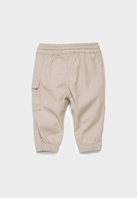 Pantalons légers beiges avec une taille élastique, ourlets à revers et une poche cargo sur le côté. Texture lisse et design simple.