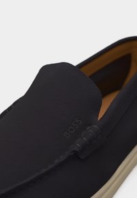 Mocassino slip-on nero con logo "BOSS" in rilievo sulla tomaia, interno color cuoio, dettagli cuciti e suola chiara.