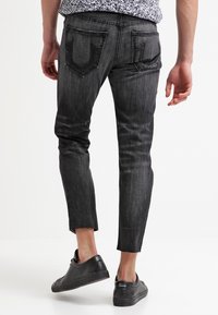Jeans de mezclilla gris con corte ajustado y dobladillo deshilachado, que cuentan con dos bolsillos traseros y un ligero desgaste en la textura. Llevados con zapatillas negras.