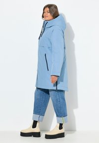 Ljust blått vattentätt jacks med en stor huva, framficka och svarta dragkedjor, kombinerat med beskurna denimjeans och beige plattformstövlar.