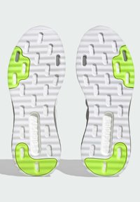 Białe podeszw sneakersów z teksturowanym gripem, z neonowo-zielonymi akcentami na pięcie i śródstopiu oraz licznymi wycięciami zapewniającymi elastyczność.