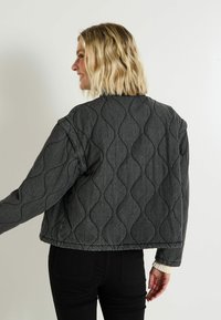 Veste en denim gris matelassée avec des motifs de vagues, coupe oversize et poignets côtelés. La vue arrière montre un col rond et des épaules tombantes.