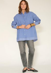 Chemise à boutons rayée bleue à manches longues, assortie à un jean gris et des ballerines noires avec des découpes circulaires. Design simple et décontracté.