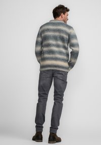 Suéter de punto a rayas azul y beige, con un cuello redondeado; combinado con pantalones gris oscuro y botas marrones, visto desde la parte de atrás.