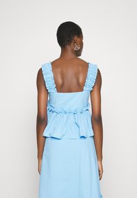 Blå randig topp med volangaxlar, en åtsittande bodice och peplumslut. Mjuk tygstruktur, baksidan visar en öppen ryggdesign.