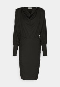 Robe noire à manches longues, longueur genou, avec un col drapé, une taille cintrée et des poignets ajustés sur un fond clair uni.