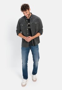 Kulfarvet skjorte med knapper og to brystlommer, båret over en sort t-shirt, parret med falmede blå jeans og hvide sneakers.