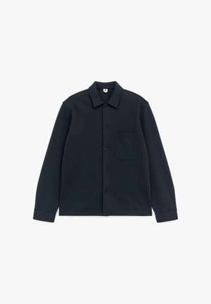 Mørkeblå langærmet skjorte med knapper, krave og enkelt brystlomme, lagt fladt ud på hvid baggrund.