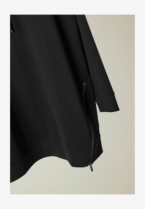 Mustapaita, jossa on sileä pinta, varustettuna vetoketjullisella sivutaskulla ja väljä istuvuus. Pitkät hihat ja kaareva helma.