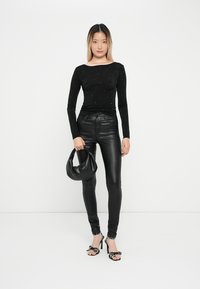 Črna majica z dolgimi rokavi z rhinestone detajli, v kombinaciji s črnimi hlačami iz umetnega usnja slim fit, črno torbico in visokimi petami s pikami.