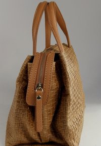 Sac en cuir tressé couleur beige avec des poignées lisses, une fermeture éclair et un motif texturé sur le corps.