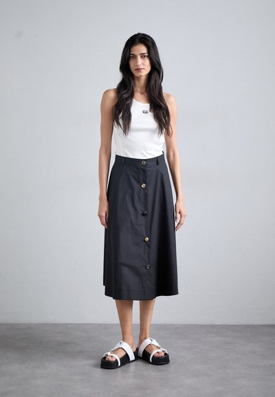 Sort midi skirt med knapdetail foran, parret med en tætsiddende hvid tanktop og chunky sorte sandaler med hvide stropper og dekorativ hardware.