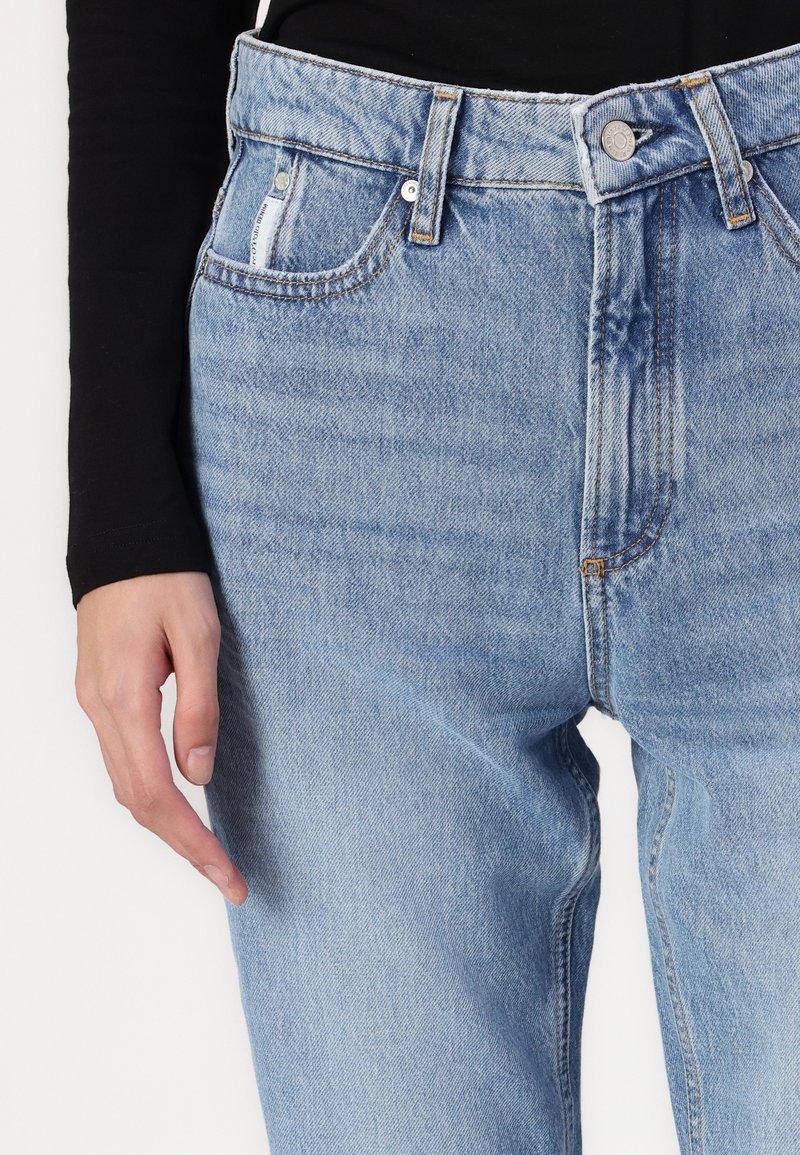 Hellblaue, hochgeschnittene Jeans mit einem lockeren Schnitt, die vordere Taschen, sichtbare Nähte und einen Knopfverschluss am Bund aufweisen.