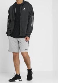 Svart zip-up hoodie med grå randiga detaljer, svart t-shirt, grå shorts och svarta sportskor; designad för aktivt bruk.