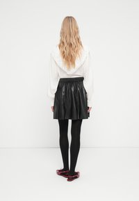 Blouse blanche avec col en dentelle, jupe en cuir noir, collants noirs et ballerines rouges. Cheveux visibles en vagues, vus de derrière.