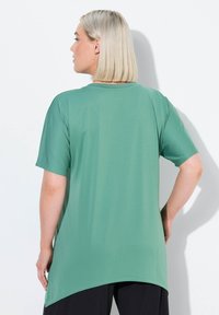 Haut à manches courtes de couleur vert menthe, en tissu texturé. Présente une coupe décontractée et un ourlet arrière plus long, avec un col ras du cou.