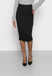 Zwarte kokerrok met een aansluitende pasvorm, met een gladde textuur zonder zichtbare patronen of versieringen, gecombineerd met zwarte hakken.