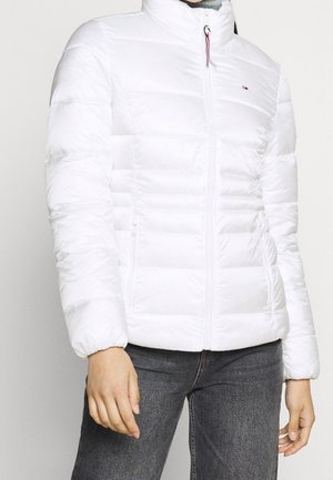 White quilted puffer jacket with front zipper and side pockets worn with dark gray jeans on a standing person.