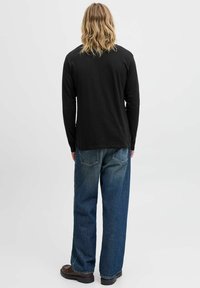 Schwarzes Langarmshirt, lockere blaue Denim-Jeans und braune Schuhe. Schlichtes Design, weicher Stoff, lässiger Schnitt, sichtbare Gesäßtaschen an den Jeans.