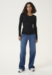 Maglietta nera a maniche lunghe con scollatura rotonda abbinata a jeans blu a gamba larga. Il tessuto è morbido ed elasticizzato, con una consistenza liscia.