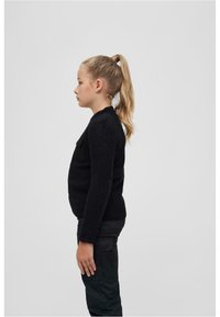 Maglione nero a maglia con scollatura rotonda, caratterizzato da una tasca a toppa sul petto e maniche lunghe, indossato sopra pantaloni cargo scuri.