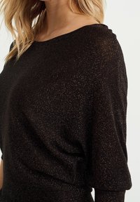 Svart, skimrande tröja med avslappnad passform, mjukt tyg och bred halsringning. Har subtila metalliska detaljer genom hela tyget.