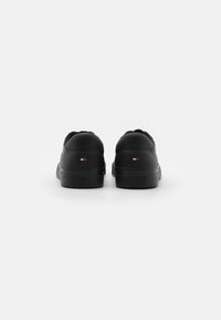 Černé tenisky s hladkým syntetickým svrškem, kulatou špičkou a plochou gumovou podešví. Zadní strana obsahuje malý detail loga v červené, bílé a modré barvě.