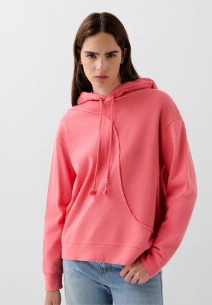 Sudadera rosa de tejido suave, con un bolsillo tipo canguro, capucha con cordón y un detalle de costura asimétrico único. Corte casual.