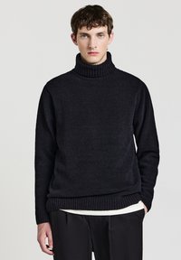 Maglione nero a collo alto in un tessuto a maglia testurizzato. Collo e orlo a coste spesse con una vestibilità rilassata, abbinato a pantaloni neri.