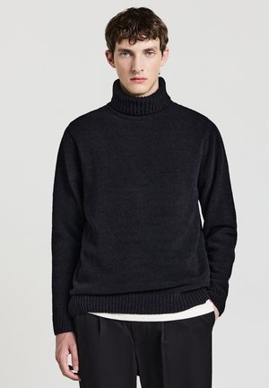 Pull noir à col roulé en tissu tricoté texturé. Encolure et ourlet côtelés épais avec une coupe décontractée, associé à un pantalon noir.