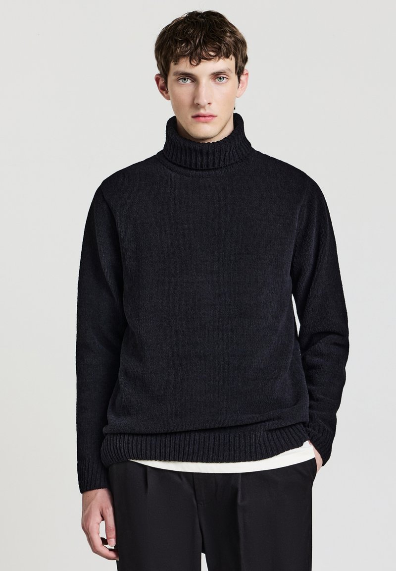 Maglione nero a collo alto in un tessuto a maglia testurizzato. Collo e orlo a coste spesse con una vestibilità rilassata, abbinato a pantaloni neri.