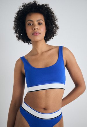 Bralette bleue et culotte assortie en tissu lisse. Dotée d'une large bande élastique avec "HUGO" en blanc et accents noirs.