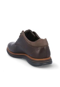 Zapato de cuero marrón con punta redondeada, acentos marrones contrastantes y una superficie texturada. Presenta una suela de goma con un ribete cosido.