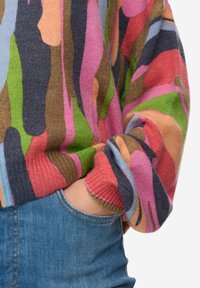 Jersey de punto colorido que presenta una mezcla de patrones abstractos en rosa, verde, azul y marrón, con puños acanalados y un corte holgado.