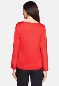 Rød, langærmet bluse med en glat, silkeagtig tekstur og rundet halsudskæring, der har en løs pasform og manchetter på ærmerne.