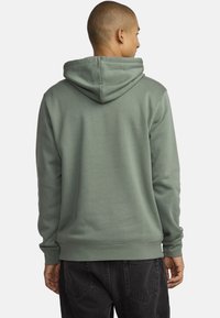 Felpa con cappuccio in morbido tessuto verde, con una vestibilità rilassata, polsini a coste e tasca a marsupio. Texture liscia con dettagli del cappuccio.