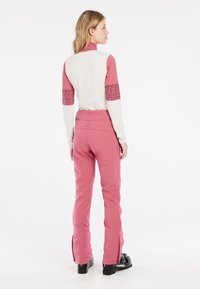 Ružový lyžiarsky oblek s priliehavým strihom, dlhými rukávmi, vysokým golierom a kontrastnými textúrovanými rukávmi. Nohavice majú zipsy pri členkoch.