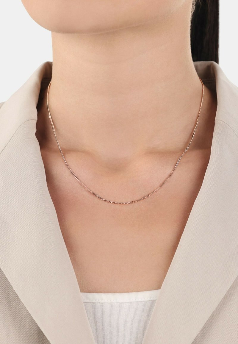 Collar de cadena de plata con un diseño delicado y delgado, descansando en el escote, combinado con una blazer beige claro y una blusa blanca.