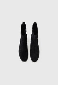 Botines de ante negro con un diseño elegante, que presentan una cremallera lateral y una textura suave, ideales para un look ceñido.
