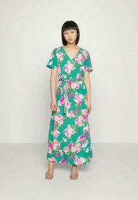Vestido maxi floral verde com mangas curtas, decote em V e cintura amarrada. Apresenta padrões de flores rosa e brancas contra um fundo verde vibrante.