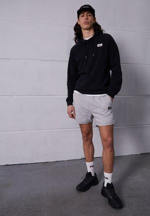 Felpa nera con logo Fila, pantaloni grigi, sneaker nere e cappellino nero. L'outfit presenta un design sportivo e casual con texture morbide.