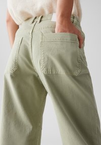 Pantalons larges vert clair en denim de coton. Comprend des poches arrière et une taille haute avec une étiquette de ceinture unie.