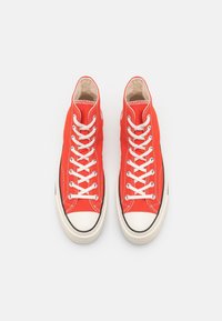 Czerwone, płócienne trampki za kostkę z białymi sznurowadłami i gumowymi noskami, z czarnymi akcentami i widocznymi detalami ściegów.