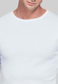Camicia bianca a maniche lunghe in morbido cotone, con scollo rotondo e design attillato, caratterizzata da una superficie liscia e priva di fantasie visibili.