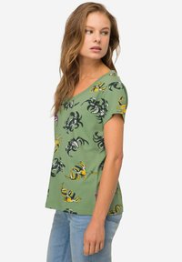 Zielony t-shirt z krótkim rękawem, zdobiony wzorem kraba w kolorze czarnym, żółtym i różowym. Z dekoltem w kształcie litery V, wykonany z miękkiego bawełnianego materiału.